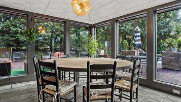 A covered patio area with a round table and chairs, large windows, and hanging plants.
