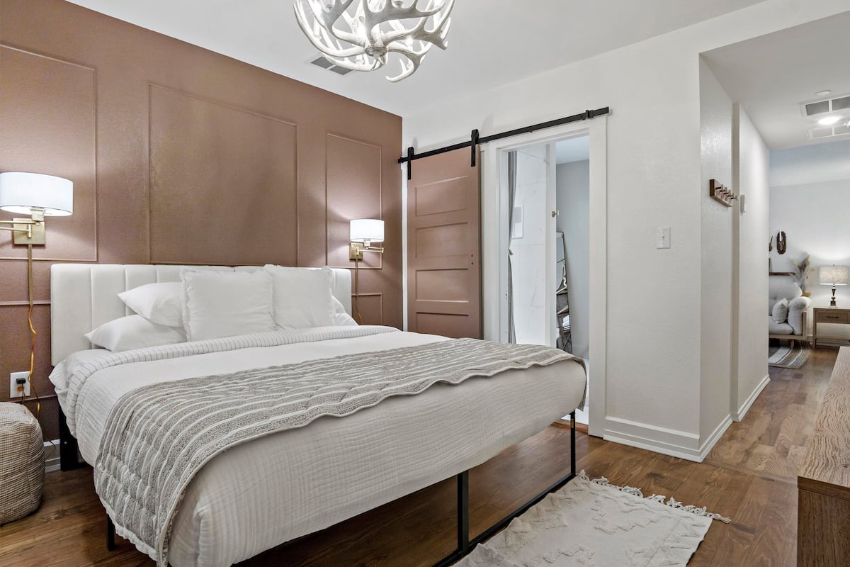 A modern bedroom with a large bed, wooden panel walls, a sliding door, and a hallway leading to a bathroom.