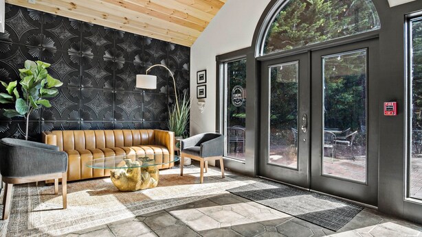 A modern lobby with a wooden ceiling, a black patterned wall, a leather sofa, a glass coffee table, and a large arched window. - Peri Social House (Black Mountain)