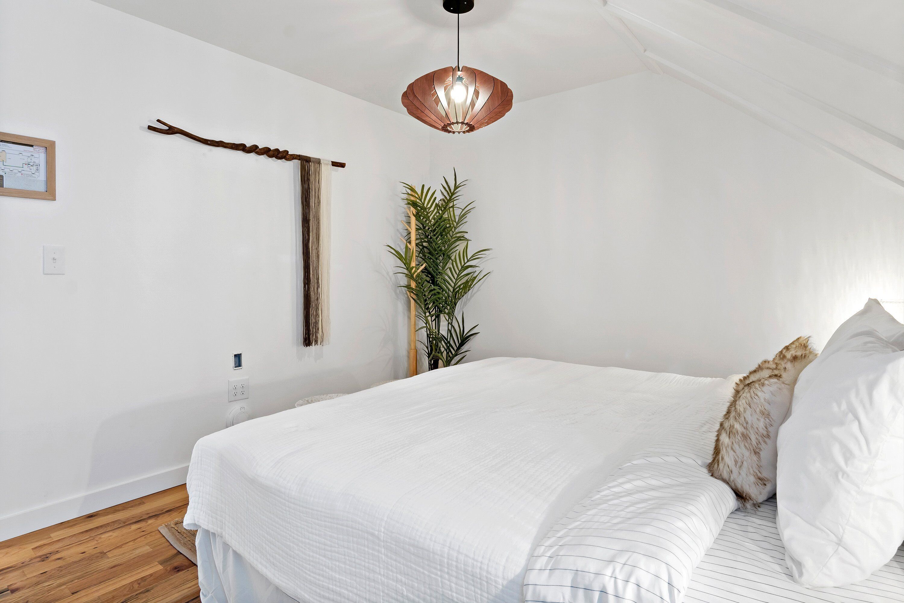 Un dormitorio con una cama grande, una lámpara colgante, una planta en la pared y una decoración de rama de madera.