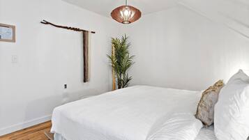 Un dormitorio con una cama grande, una lámpara colgante, una planta en la pared y una decoración de rama de madera.