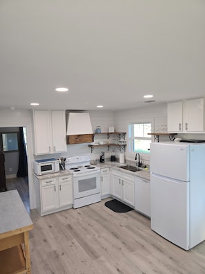 Una cocina moderna con armarios blancos, horno empotrado, microondas y refrigerador.