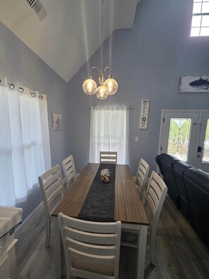 A dining area with a wooden table, white chairs, a black runner, and a chandelier.