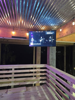 Una terraza de madera con una pantalla de televisión mostrando a una banda actuando.