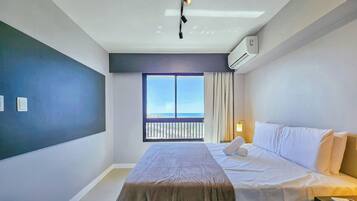 A hotel room with a bed, a window with a view, an air conditioning unit, and a ceiling light fixture.