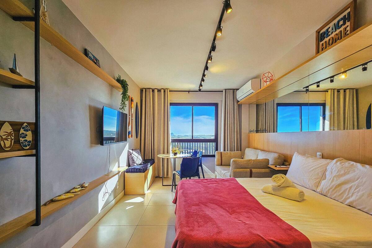 Habitación de hotel con cama, escritorio, silla, sofá, televisor y ventana grande.