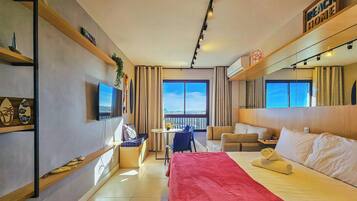 Habitación de hotel con cama, escritorio, silla, sofá, televisor y ventana grande.