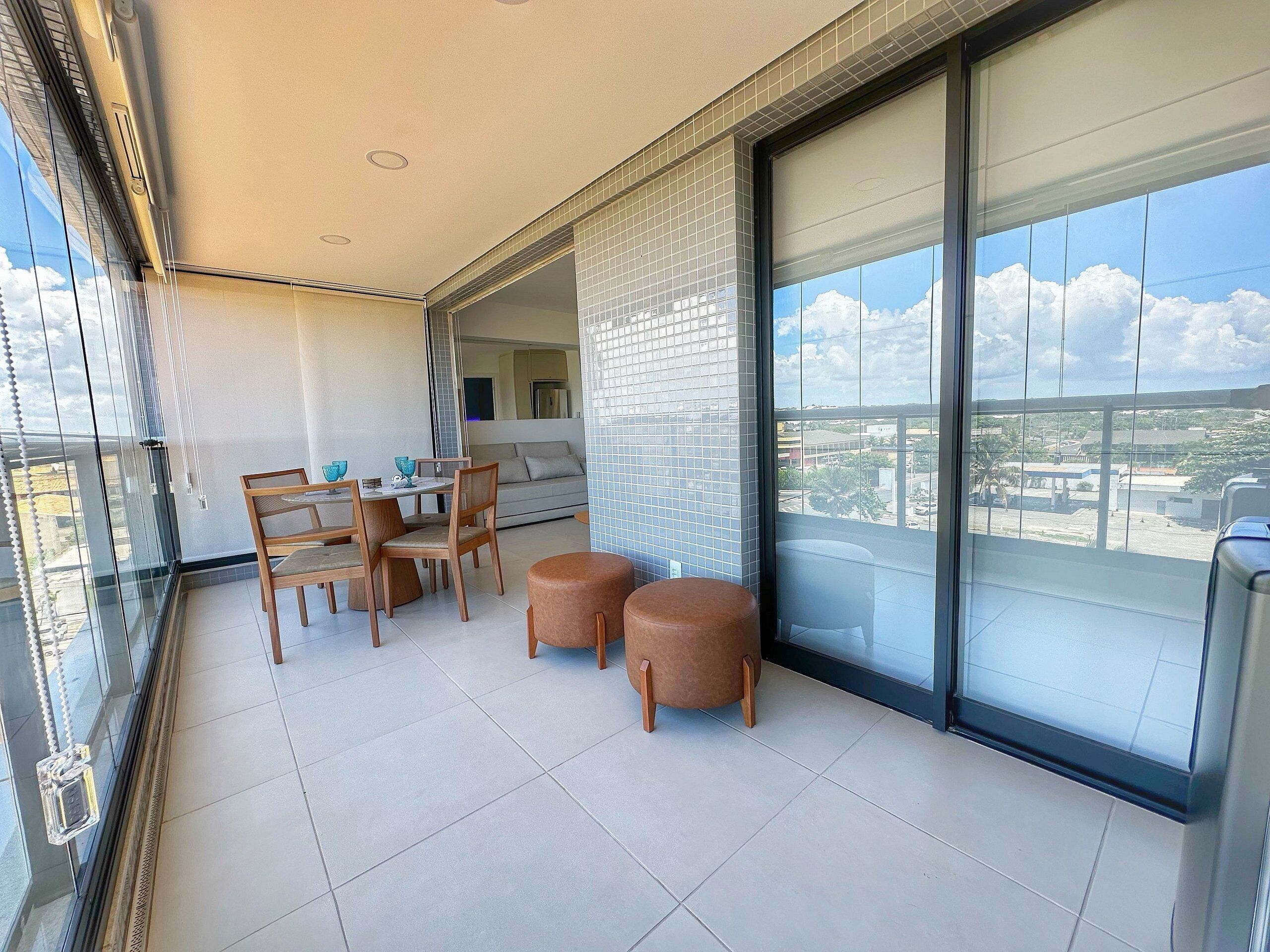 A balcony with a dining table, chairs, and ottomans.