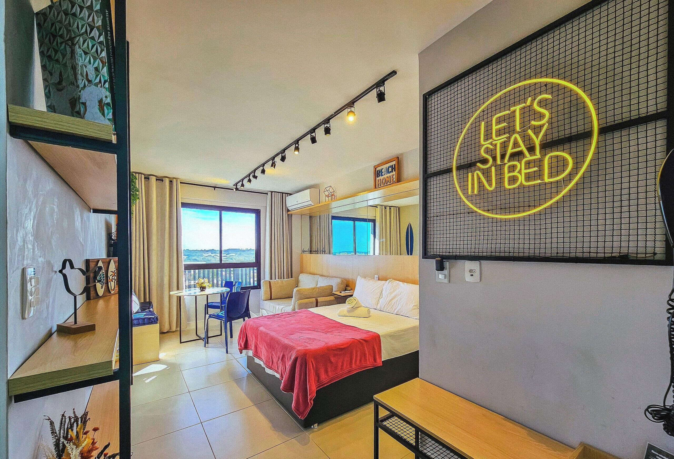 Habitación de hotel con cama, escritorio, silla, ventana con vista y un letrero de neón en la pared.