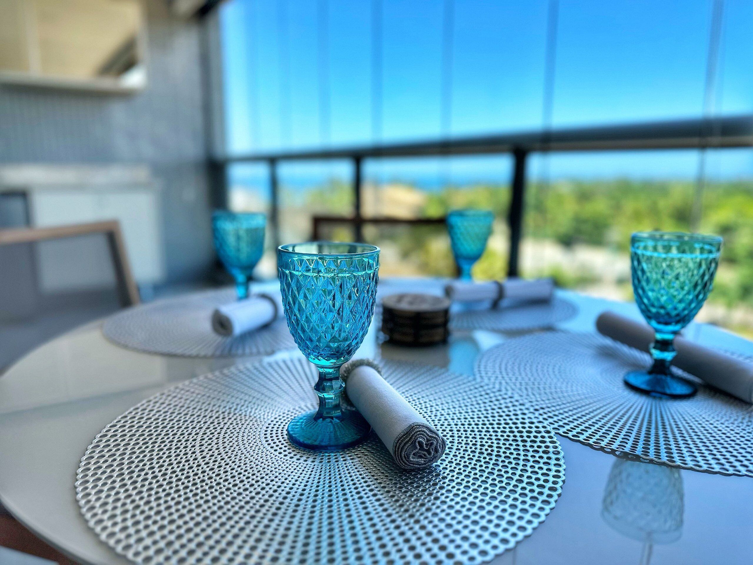 A table with blue glassware and a rolled towel, set on a perforated table mat.