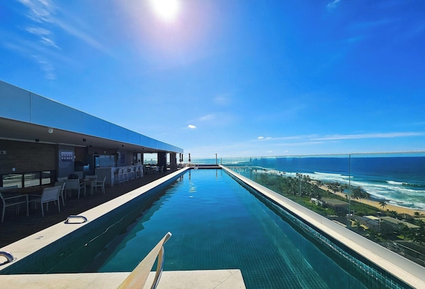 A long swimming pool with a view of the ocean and a beach. - Premium Stella Maris by VLV Stays (Salvador)