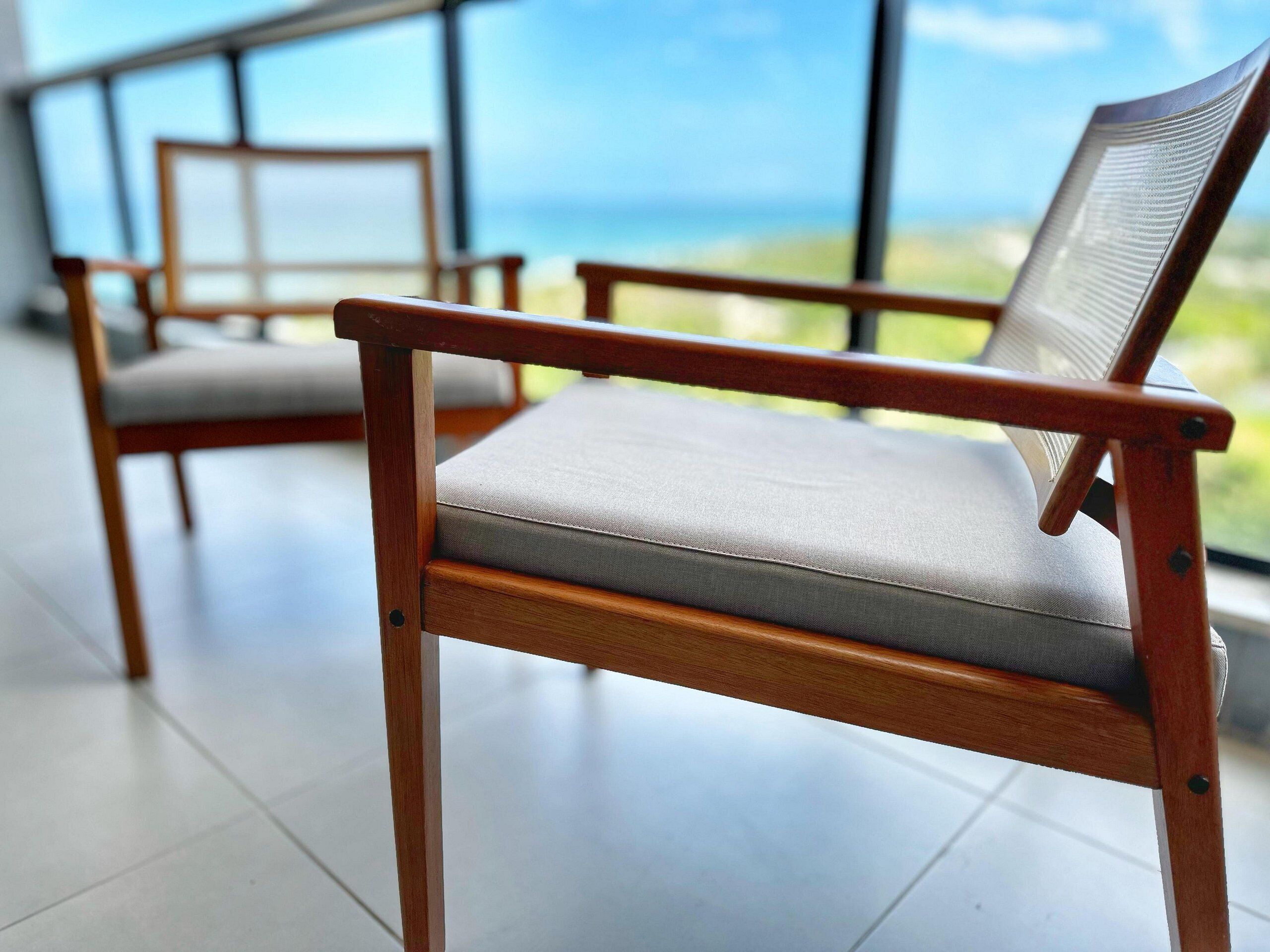 A wooden chair with a grey cushion in a room with a large window.