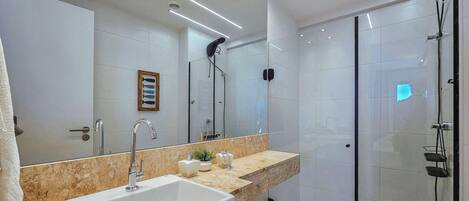 A modern bathroom with a large sink, mirror, and glass shower enclosure.