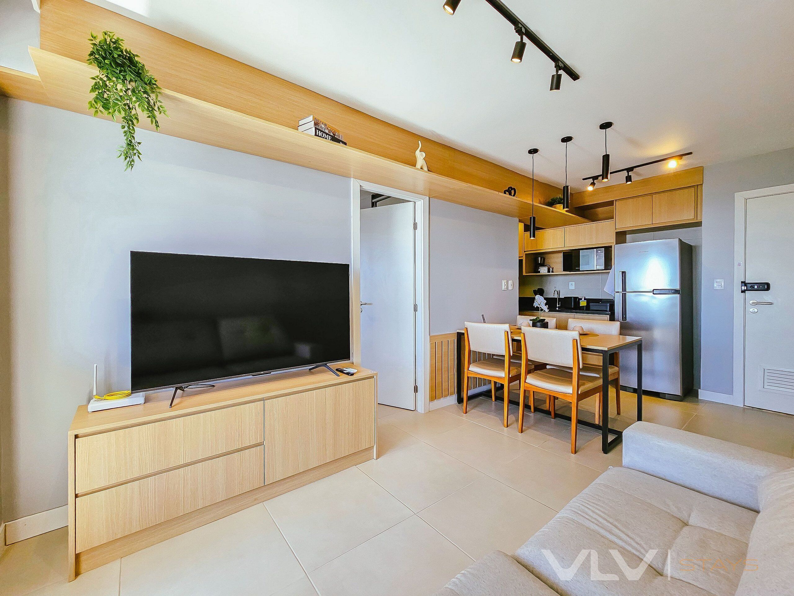 A modern living room with a flat-screen TV, wooden furniture, and a dining area with chairs and a table.
