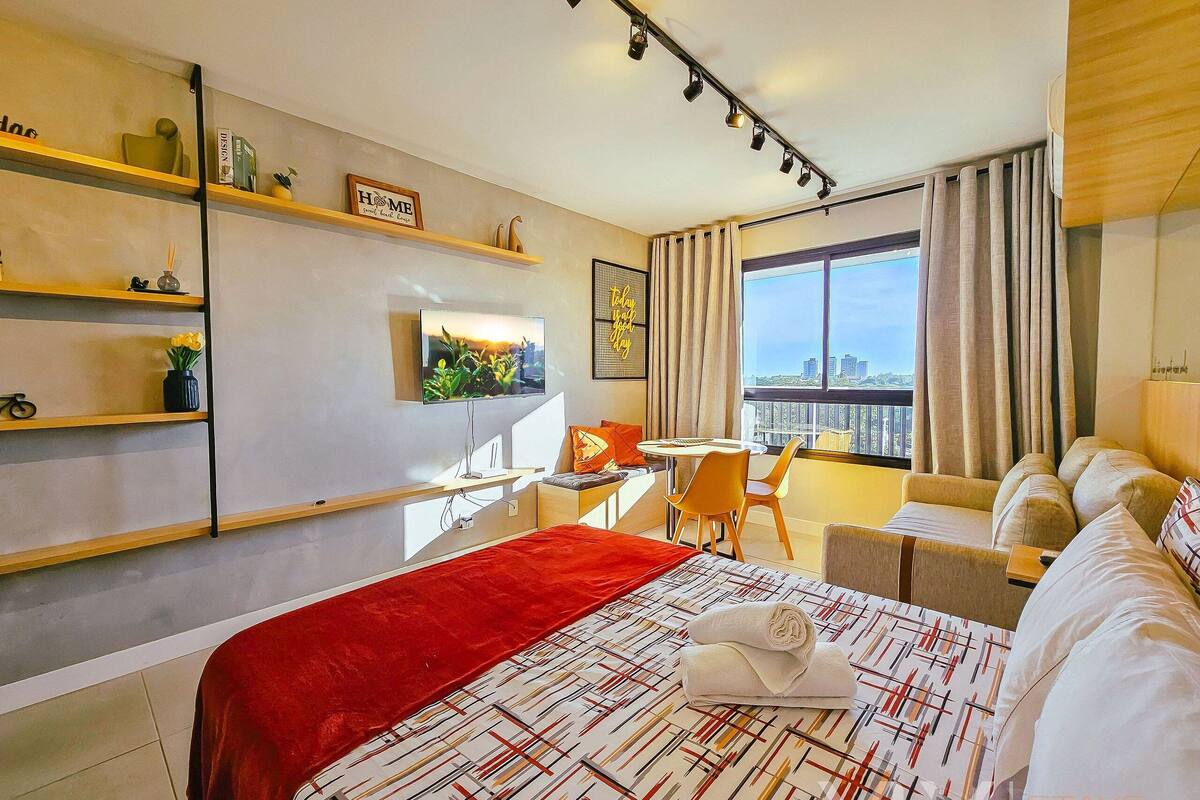 Habitación de hotel con cama, escritorio, silla, sofá, televisor y ventana con vista a la ciudad.