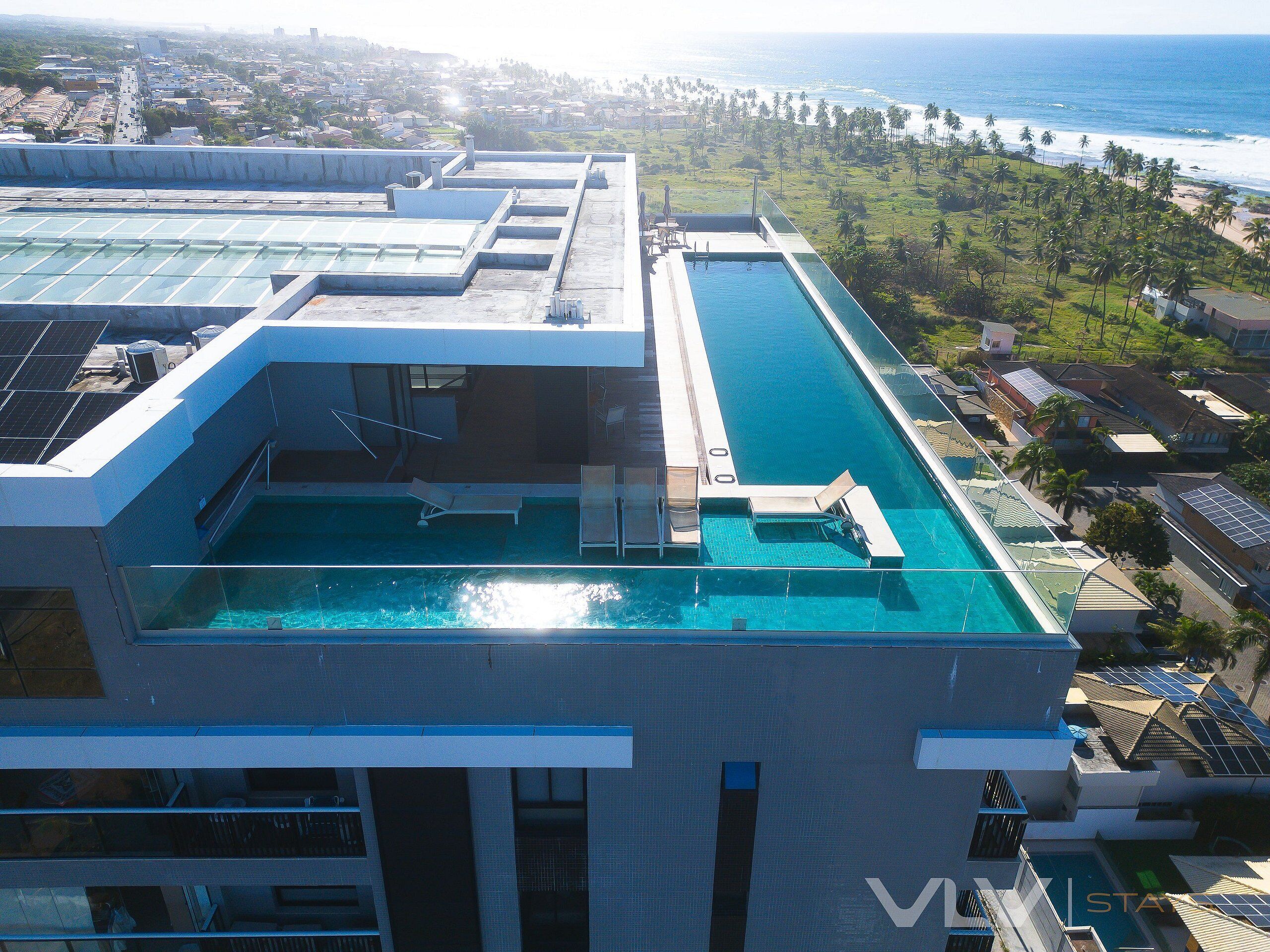 A rooftop pool with a glass barrier, lounge chairs, and a view of the ocean.