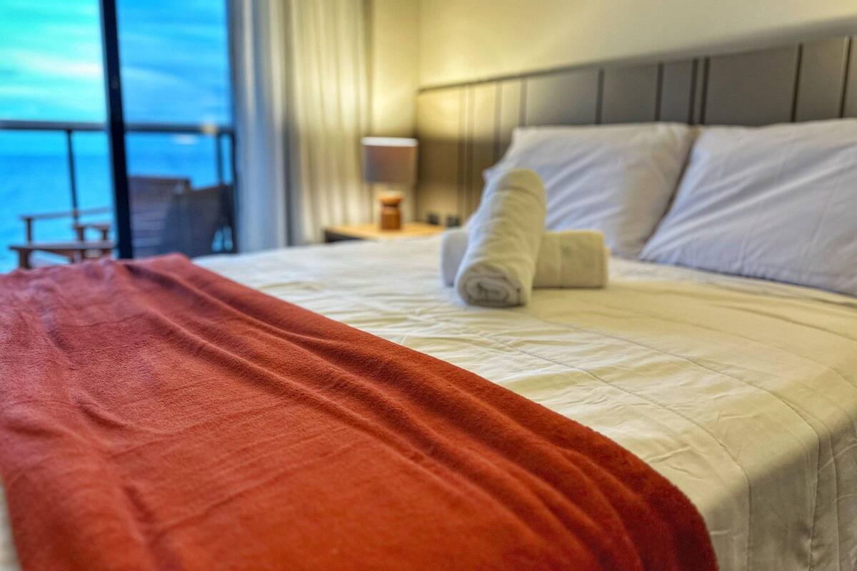 Una habitación de hotel con cama, vista al océano y balcón.