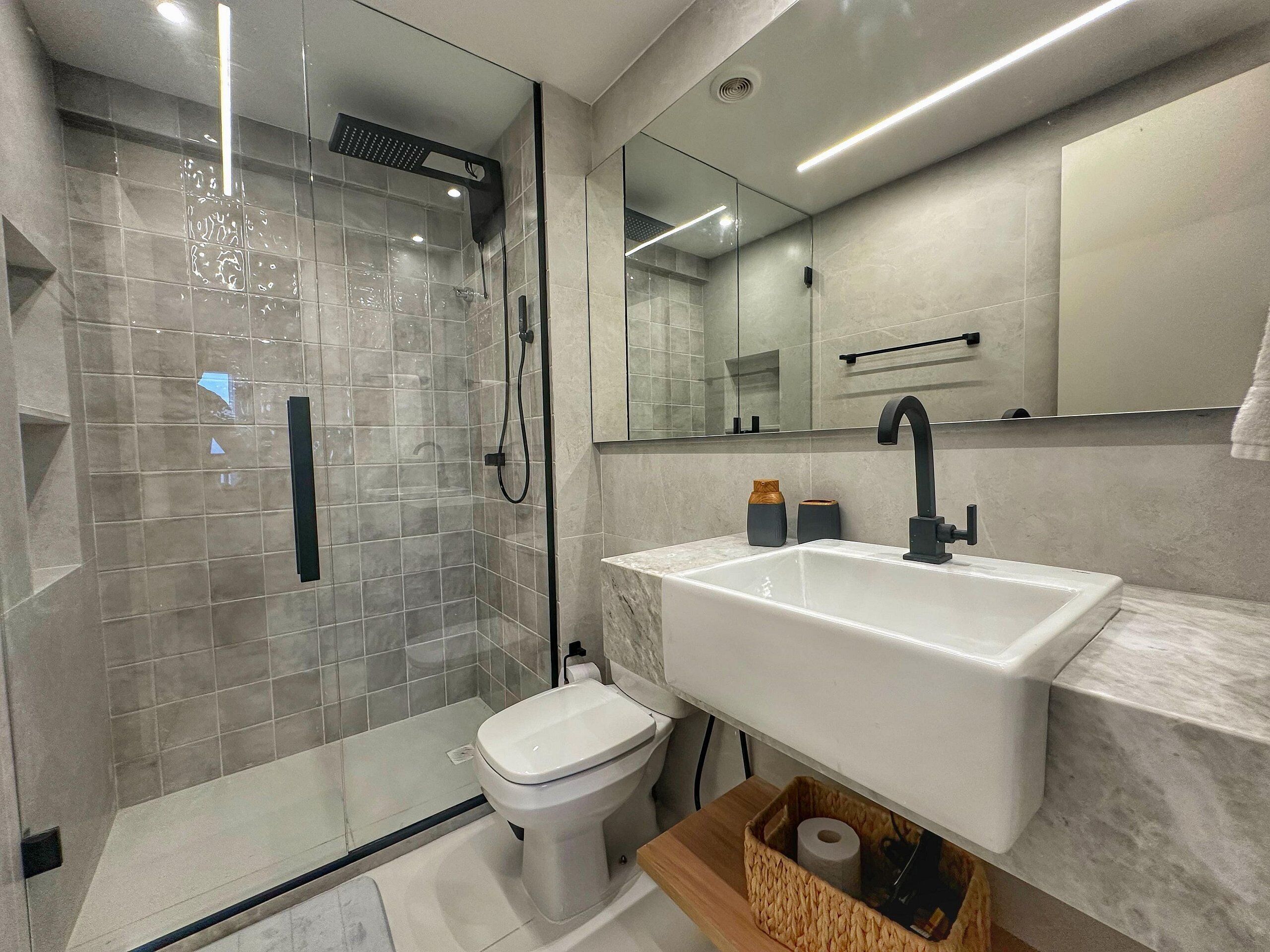 A modern bathroom with a glass shower enclosure, a white sink, and a toilet.