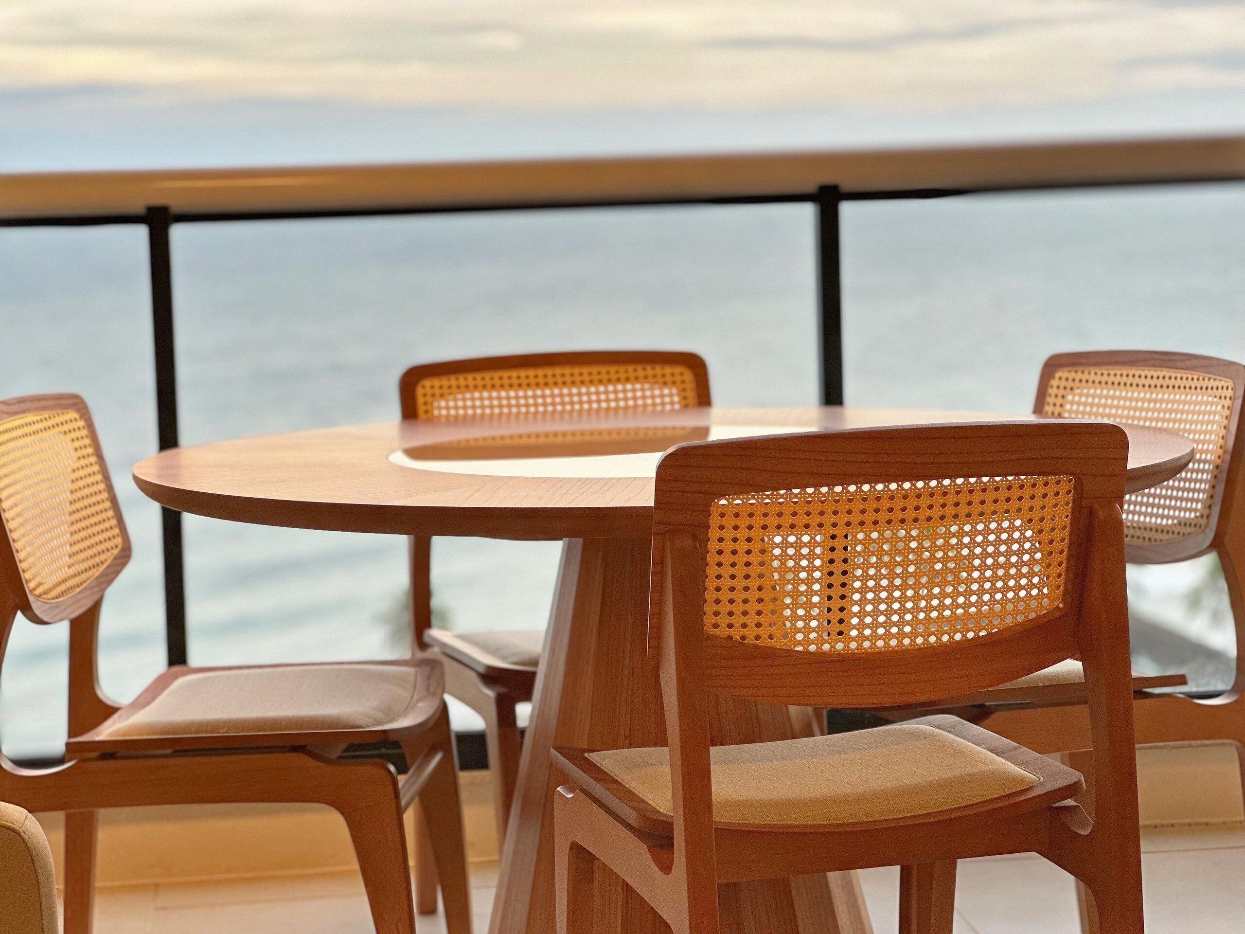 Ein runder Holztisch mit vier Korbstühlen, auf einem Balkon mit Blick auf das Meer.