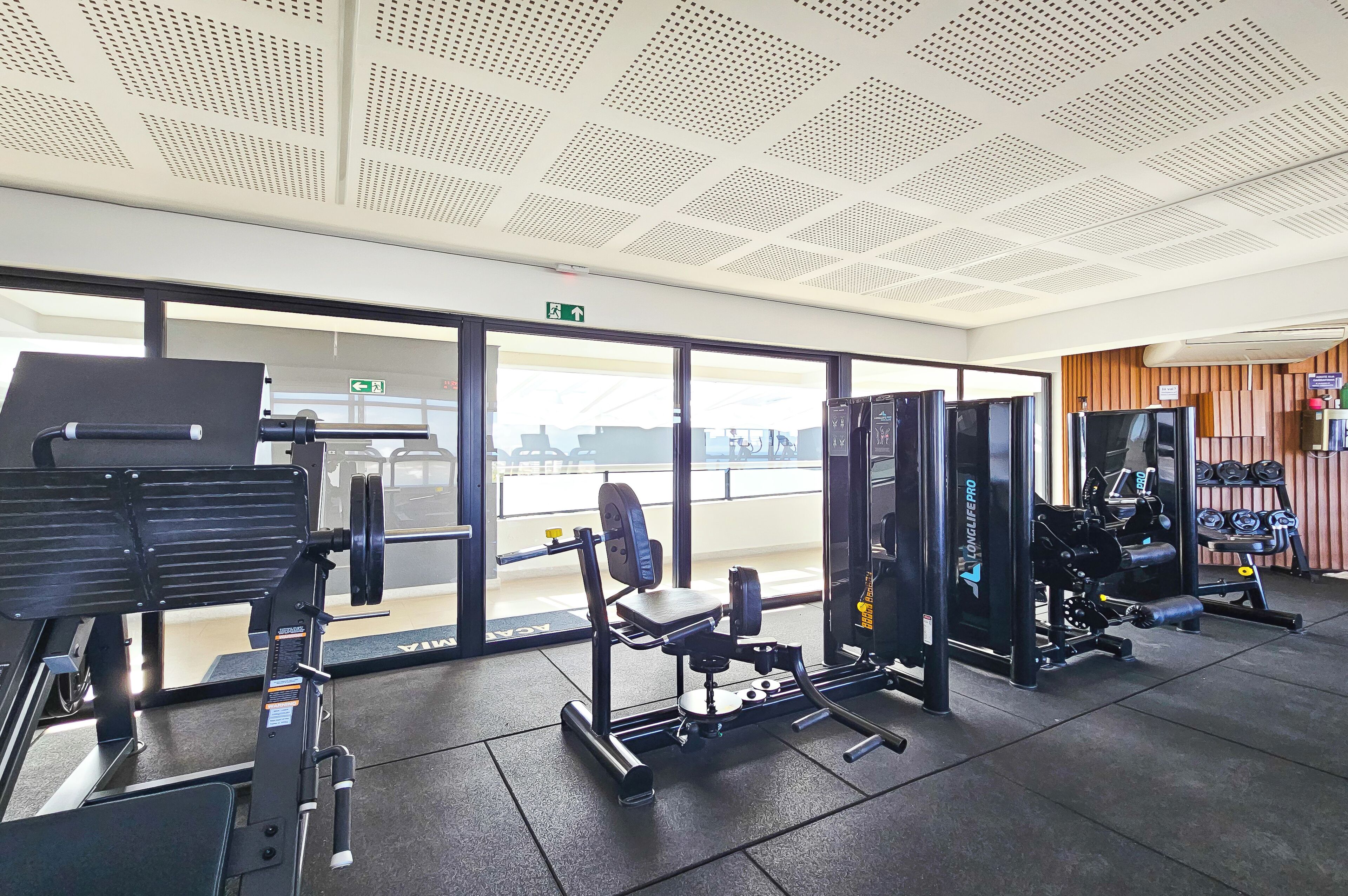 Une salle de sport équipée de divers appareils d’exercice, dotée d’une grande fenêtre et d’un plafond orné d’un motif en réseau.