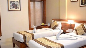 Une chambre d’hôtel avec deux lits, chacun doté d’un porte-serviettes, d’une tête de lit en bois et d’une petite table avec une lampe.