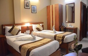 A hotel room with two beds, wooden headboards, a desk with a mirror, and a vase with flowers. - Hotel Eden roc (Bhubaneshwar)