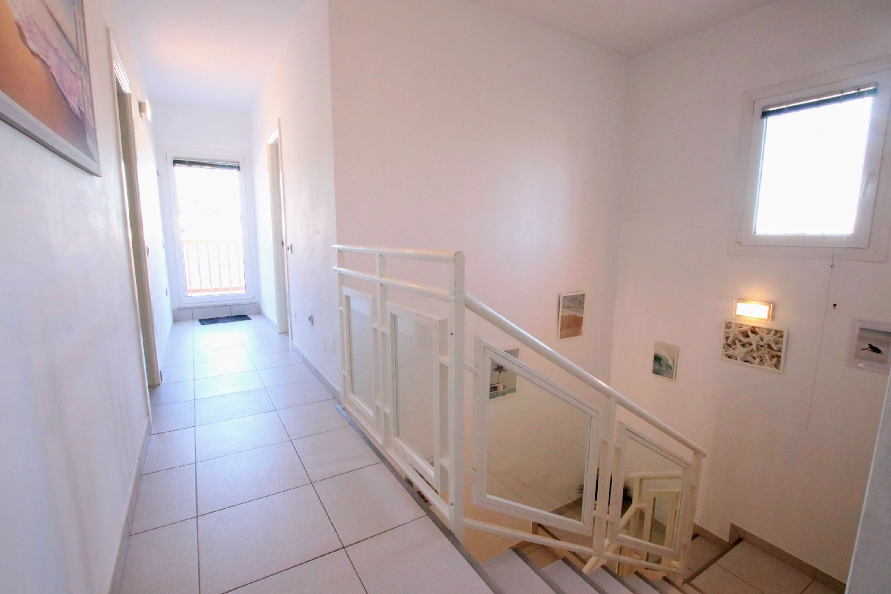 A clean, white-walled hallway with a tiled floor leading to a staircase with a white railing.
