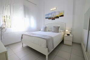 Un dormitorio con una cama blanca, mesitas de noche y una lámpara de pared.