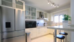 Une cuisine moderne dotée d’appareils électroménagers en acier inoxydable, de meubles blancs et d’un coin bar avec des tabourets.
