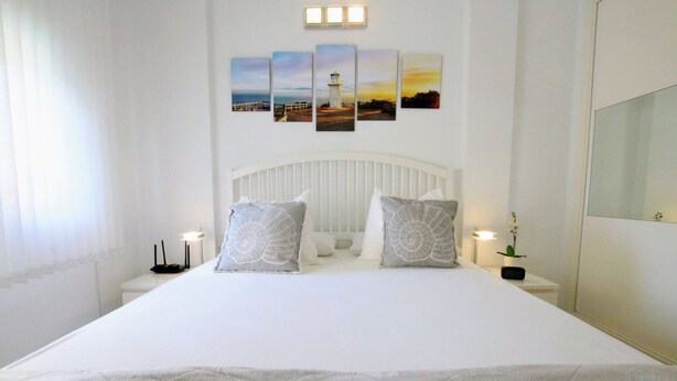 Une chambre à coucher avec un grand lit, une tête de lit blanche et un mur orné de quatre tableaux encadrés.