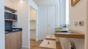 A compact kitchen with a microwave, wooden cabinets, a small wooden stool, and a countertop with a wine glass and plates. - Studio San Michele by Wonderful Italy (Turin)