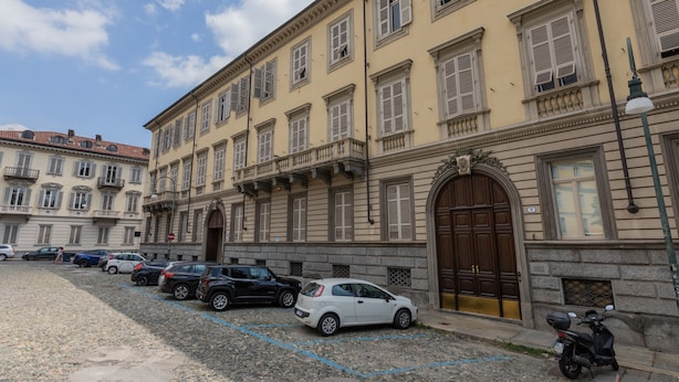 A row of parked cars in front of a building with a large arched entrance and multiple windows. - Studio San Michele by Wonderful Italy (Turin)