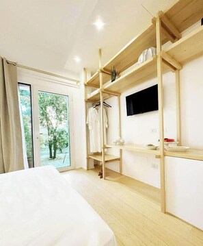 A hotel room with a bed, a wooden wardrobe, a TV mounted on the wall, and a view of trees through the window. - Euphony, Short Room (Lecce)