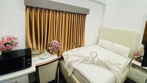 Une chambre d’hôtel équipée d’un lit, d’un bureau avec un micro-ondes, d’une chaise, d’une télévision et d’un ventilateur de plafond.