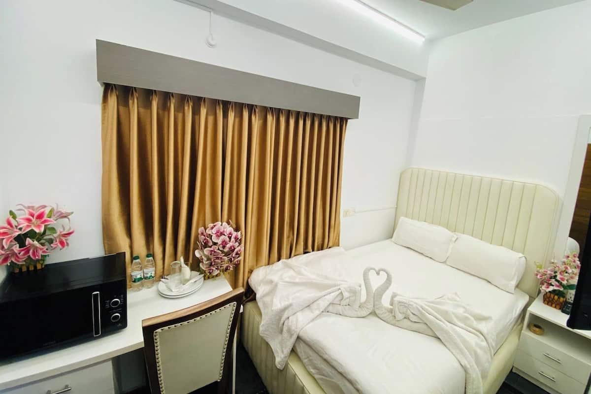 Une chambre d’hôtel équipée d’un lit, d’un bureau avec un micro-ondes, d’une chaise, d’une télévision et d’un ventilateur de plafond.