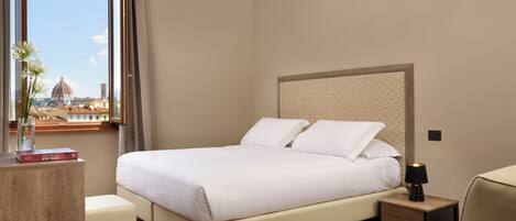 Hotelkamer met een bed, nachtkastje, lamp en raam met uitzicht op een koepel en gebouwen.