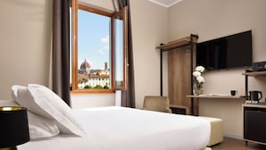 Hotelkamer met een bed, een bureau met een flatscreen televisie, een stoel en uitzicht op een gebouw met een koepel.