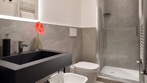 Een moderne badkamer met een zwart wastafel, een wit toilet en een douche met glazen wanden.
