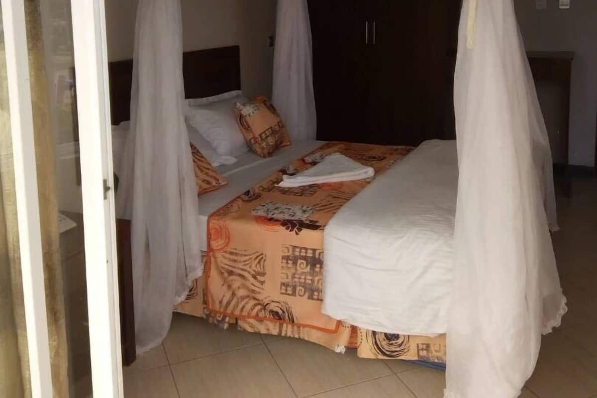 A bedroom with a bed covered in a patterned bedspread, white curtains, and a canopy.