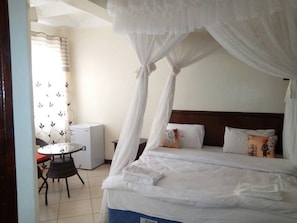 Un dormitorio con cama con dosel, una pequeña mesa con sillas y un refrigerador.