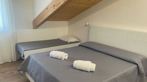 Une chambre avec deux lits, des poutres apparentes en bois au plafond, des murs blancs et un sol carrelé.