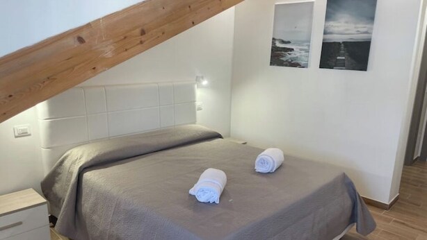 Une chambre à coucher avec un lit, deux serviettes enroulées, une table de chevet, une poutre en bois au plafond et deux tableaux encadrés accrochés au mur.
