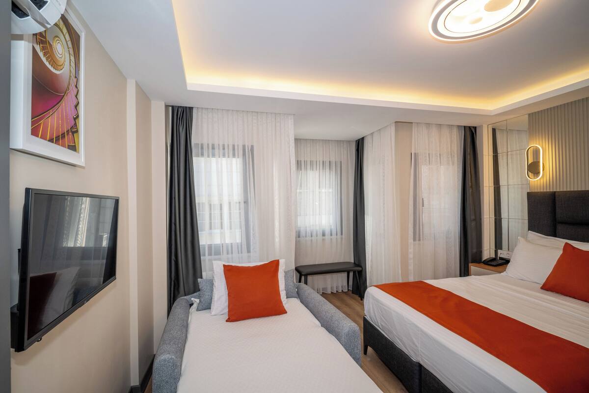 A modern hotel room with a large bed, a bedside table, a TV, and a mirror.