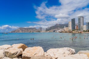 A coastal cityscape with clear blue waters, rocky shoreline, and modern buildings.