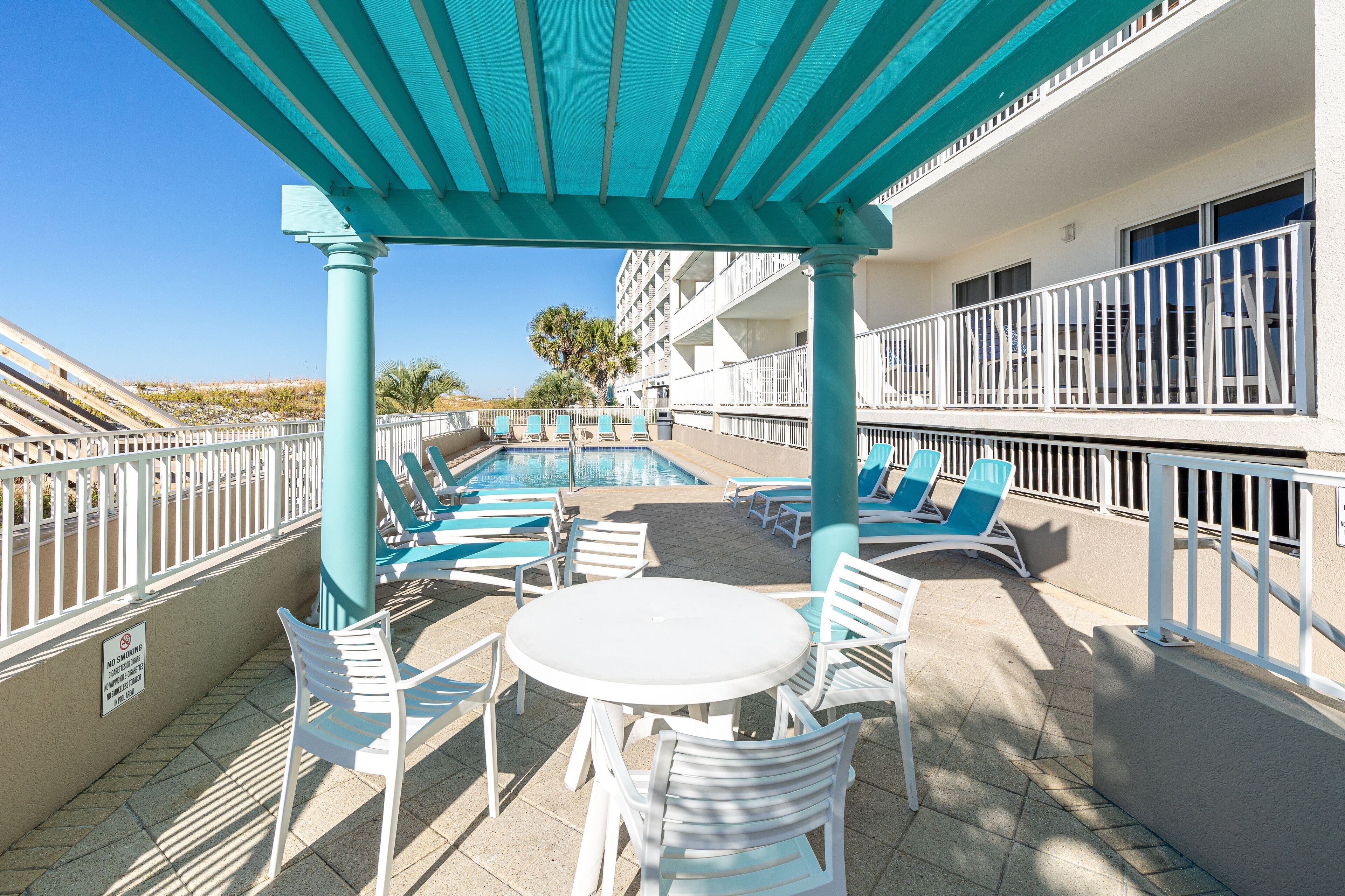 A poolside area with lounge chairs, a table, and a covered seating area.