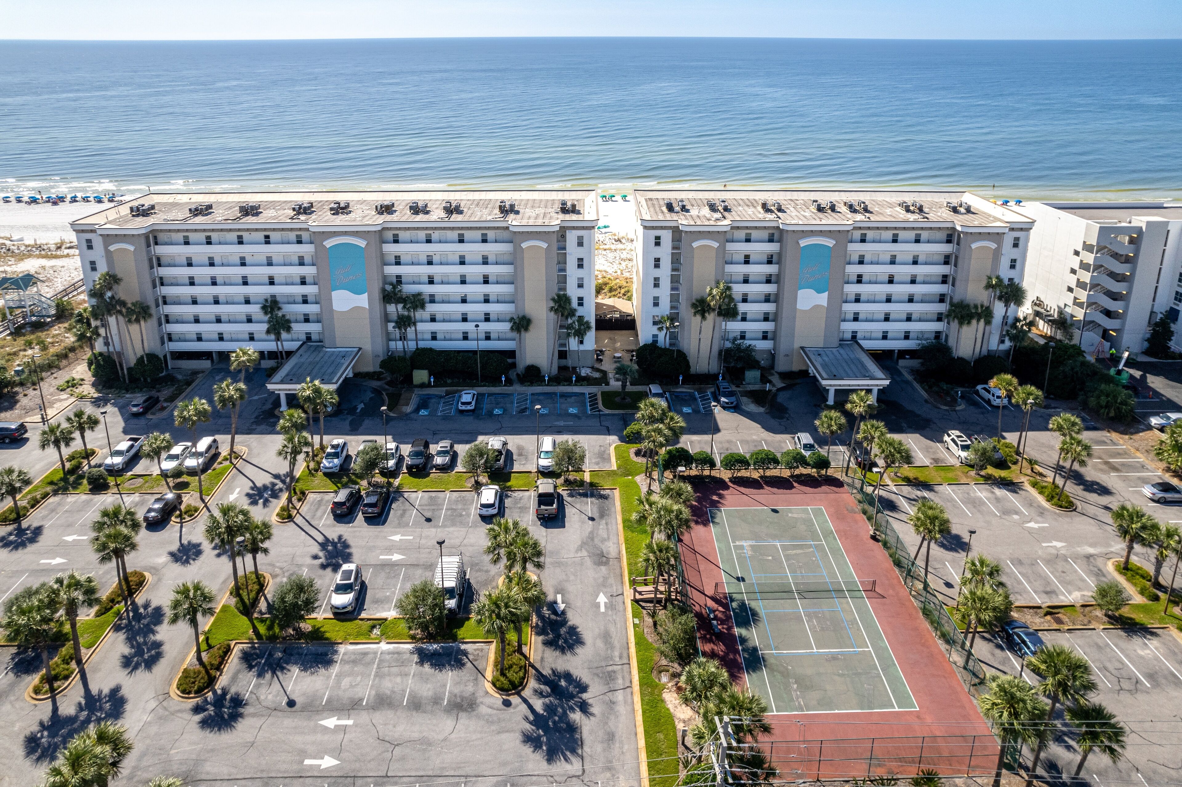 A hotel with multiple floors, a parking lot, and a tennis court.