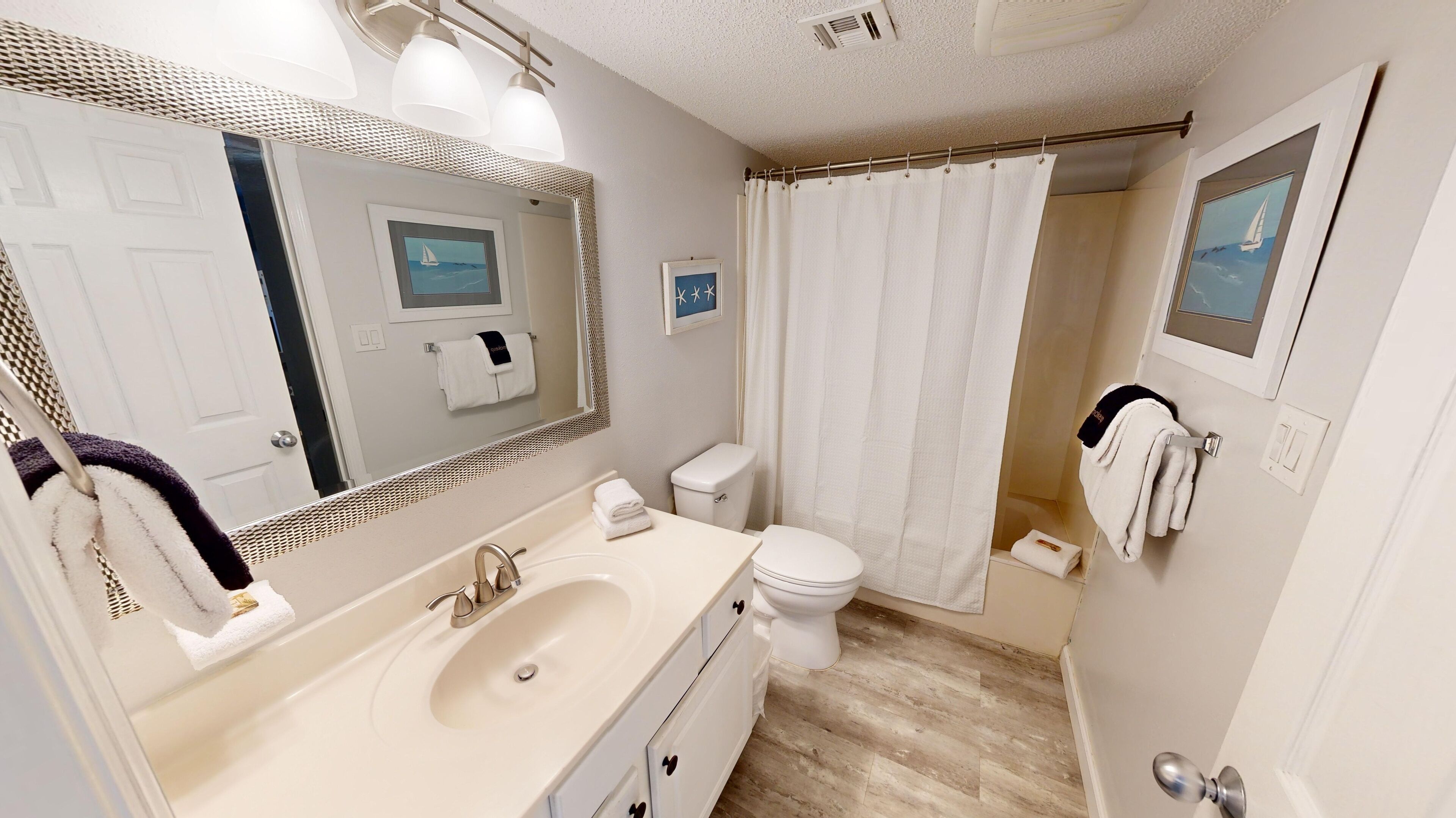 A bathroom with a sink, mirror, toilet, and shower curtain.