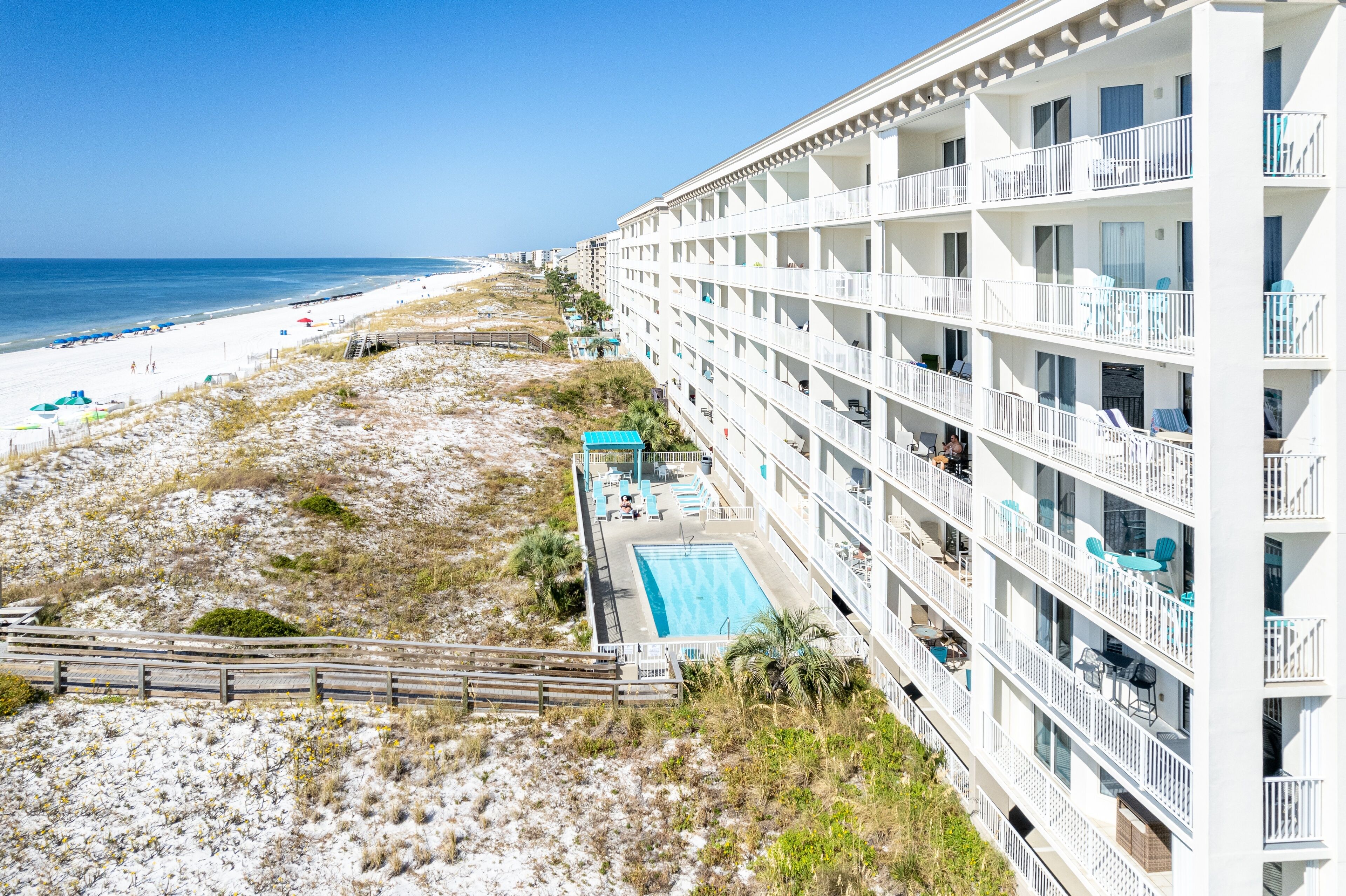 A beachfront hotel with multiple balconies, a swimming pool, and a beach view.