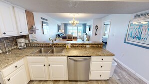A modern kitchen with granite countertops, white cabinetry, and a built-in dishwasher. - Gulf Dunes 102 3 Bedroom Condo by RedAwning (Fort Walton Beach)