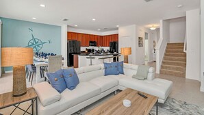 A modern living room with a sectional sofa, dining area, kitchen, and staircase. - Upstay: Resort Villa w Pool & Cinema near Disney (Kissimmee)